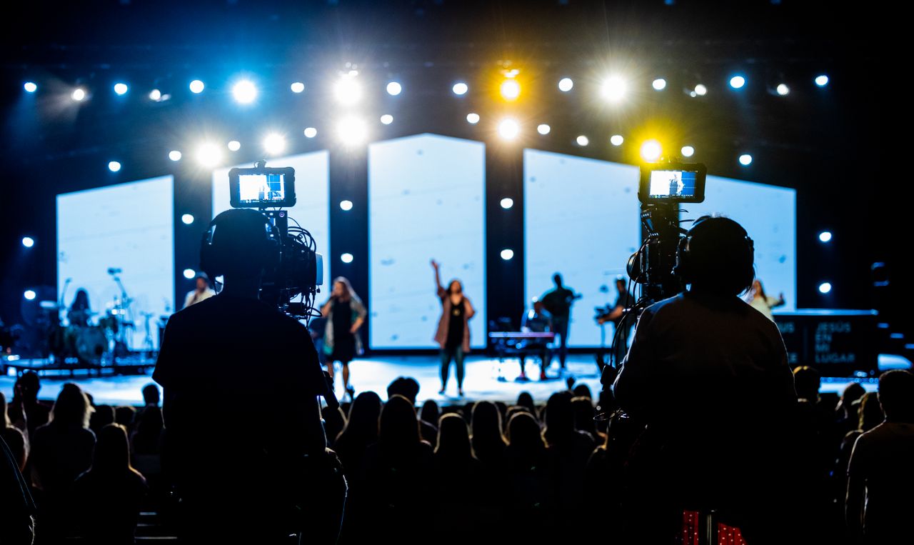 Energetic live concert scene with cameramen filming the vibrant stage performance.